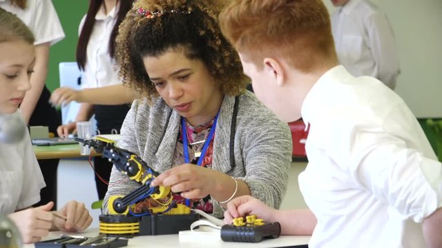 Students are learning about a robotic arm they are building with their teacher.