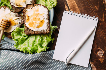 Notebook with a pen on the table next to sandwich