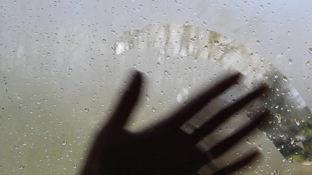Une main nettoie la vitre embuée après la pluie