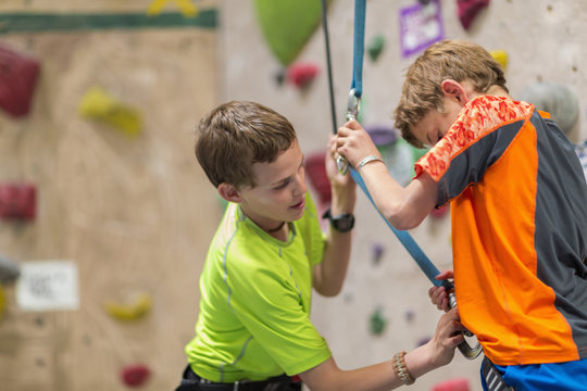 Caucasian boy fastening harness of boy near rock wall
