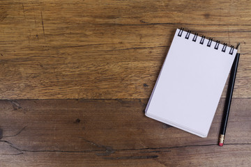 White sheets notebook with spiral on right side of the wooden dark brown table with black pencil aside from above