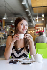 Beautiful girl in a cafe drinking tea, coffee, breakfast the restaurant looking out into street