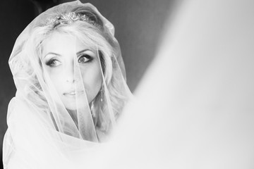 Beautiful emotional blonde bride posing under veil, face closeup