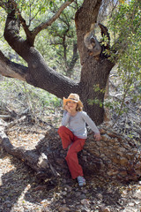 Naklejka na ściany i meble Girl in cowboy hat sitting under a tree on a rock