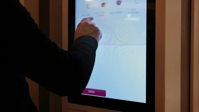 A person uses the touchscreen menu for odering some food in a fast-food restaurant