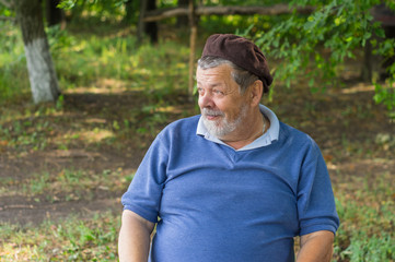 Outdoor portrait of bearded smiling senior man in a tree shadow