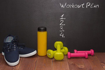 Fitness shoes, dumbbells and bottle of juice on wooden floor