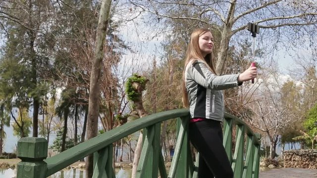 Young happy woman taking self portrait standing on the wooden bridge using smartphone mobile cell phone camera. Closeup. HD 1920x1080.
