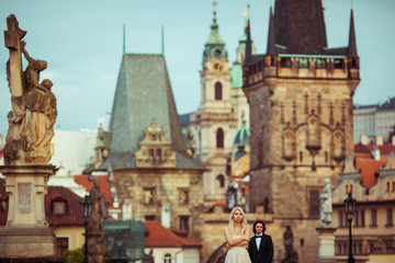 Fototapeta na wymiar Beautiful blonde bride & handsome groom posing on Prague bridge,