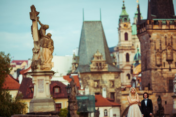 Fototapeta na wymiar Beautiful blonde bride & handsome groom posing on Prague bridge,