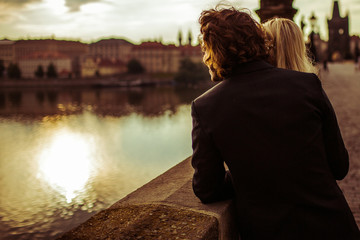 Fototapeta na wymiar Romantic newlyweds hugging on bridge in Prague, looking at river
