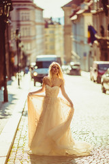 Naklejka premium Beautiful fairytale blonde bride posing in empty street at sunri