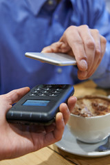 Man Using Contactless Payment App On Mobile Phone In Cafe