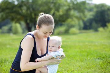 Caring mother is holding the baby, against summer park