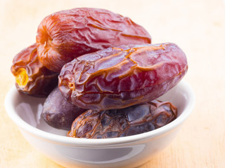 sweet dry date palm fruit on white dish on wood