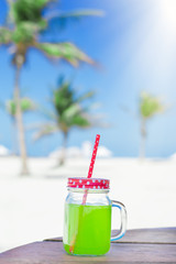 Green juice in a glass jar with a red funny straw, palm trees and blue sky