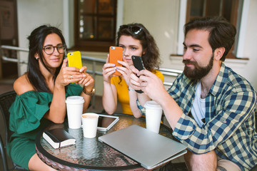 Young friends with smartphones and laptop in cafe with coffee