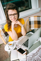 Girl in glasses with laptop and tea in cafe outdoors