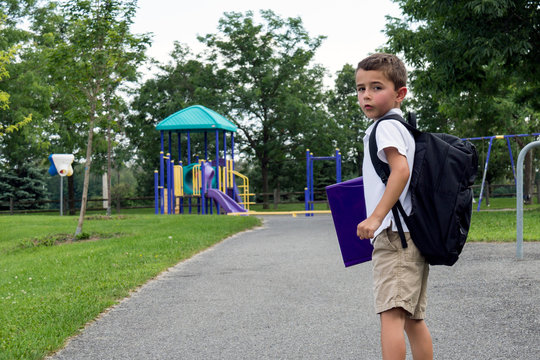 Child with school backpack and book walking in the park