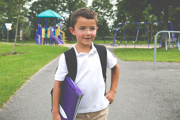 Little boy with school backpack and book in the play yard lookin