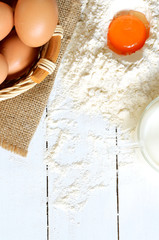 Eggs, flour, yolk, milk and canvas bag on white wooden desk