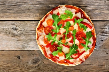 Homemade pizza with arugula and cherry tomatoes against a rustic wood background