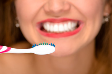 Closeup young womans mouth showing white healthy teeth and holding toothbrush in front