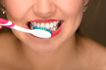 Closeup young womans mouth and white teeth, using toothbrush