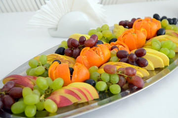 Vegetarian food. A dish with mixed fruit on the holiday table. Bananas and apples, grapes and oranges on a platter. Healthy food for dessert.