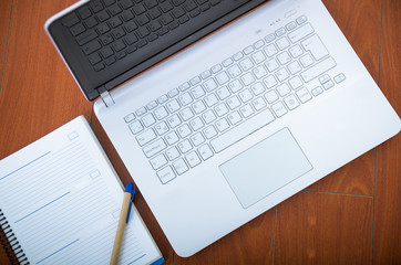 White laptop as seen from above sitting on wooden surface with notepad and pen next to it