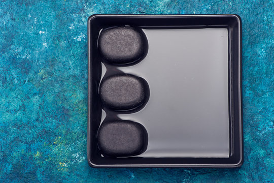 Black zen stones in a bowl of water. Spa set