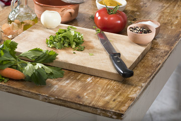 Chop celery, tomato, onions on a wooden cutting board for cooking.