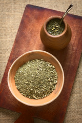 South American yerba mate (mate tea) dried leaves in clay bowl with a wooden mate cup filled with tea photographed with natural light. Mate is the national infusion of Argentina.