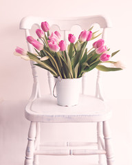 Pink and white tulips in a vintage white tin bucket on a chair