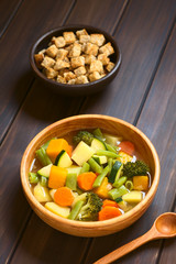 Vegetable soup made of zucchini, green bean, carrot, broccoli, potato and pumpkin, croutons in the back, photographed with natural light (Selective Focus, Focus one third into the soup)