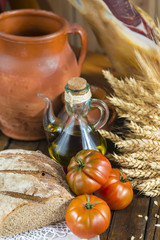 Bodegón de comida con aceite de oliva, pan, tomates, jamón y espigas de cereales en ambiente rústico