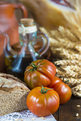 Bodegón de comida con aceite de oliva, pan, tomates, jamón y espigas de cereales en ambiente rústico