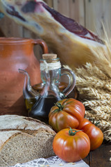 Bodegón de comida con aceite de oliva, pan, tomates, jamón y espigas de cereales en ambiente rústico