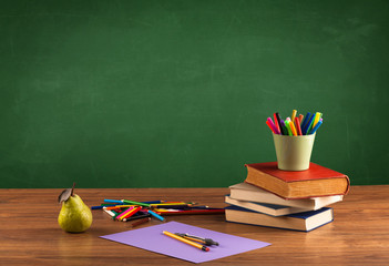 School items on desk with empty chalkboard