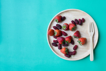 Strawberries and mulberries on wooden plate with copy space on aqua background