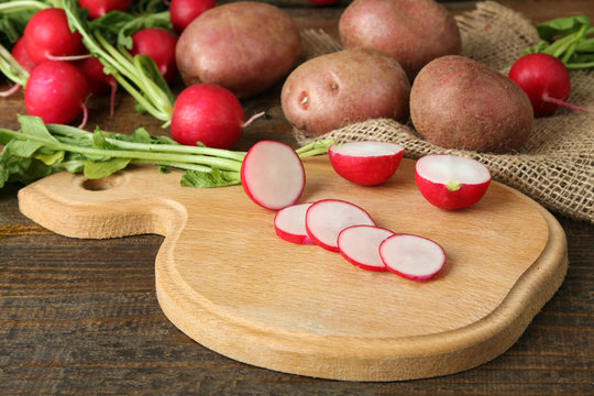 red potatoes on wooden brown background near a cutting Board with sliced radishes on wooden brown background