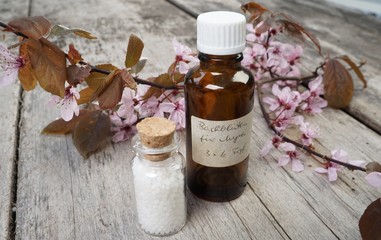 Globuli mit Bachblüten und Kirschblüten auf rustikalem Tisch 