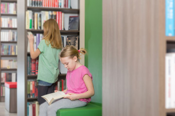 Fototapeta premium Cute two girls reading book in library