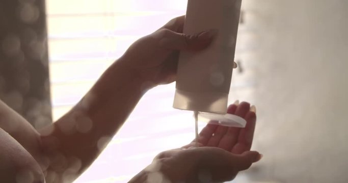 Naked woman pouring hair shampoo on her hand 