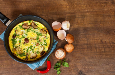 omelet with mushrooms in a frying pan on wooden table