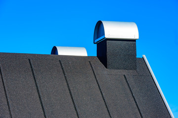 Rooftop with covered chimneys. Roof is black and covered in tar paper or roofing felt. Blue sky in background. - 107584057