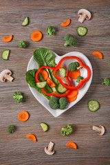 Useful cut vegetables on a plate in the form of heart on wooden table top view