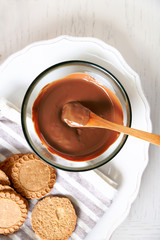 Melted chocolate on glass bowl, on wooden background