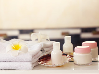 Fototapeta na wymiar White towels with cream and tropical flower on a shelf in bathroom