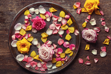 Pink and yellow rose petals in silver bowl with water on wooden background